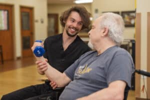 A physical therapist helping a man lift weights at Pine Ridge